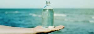 Propiedades del agua de mar: botella de agrua sobre mano extendida y el mar al fondo