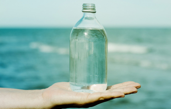Propiedades del agua de mar: botella de agrua sobre mano extendida y el mar al fondo