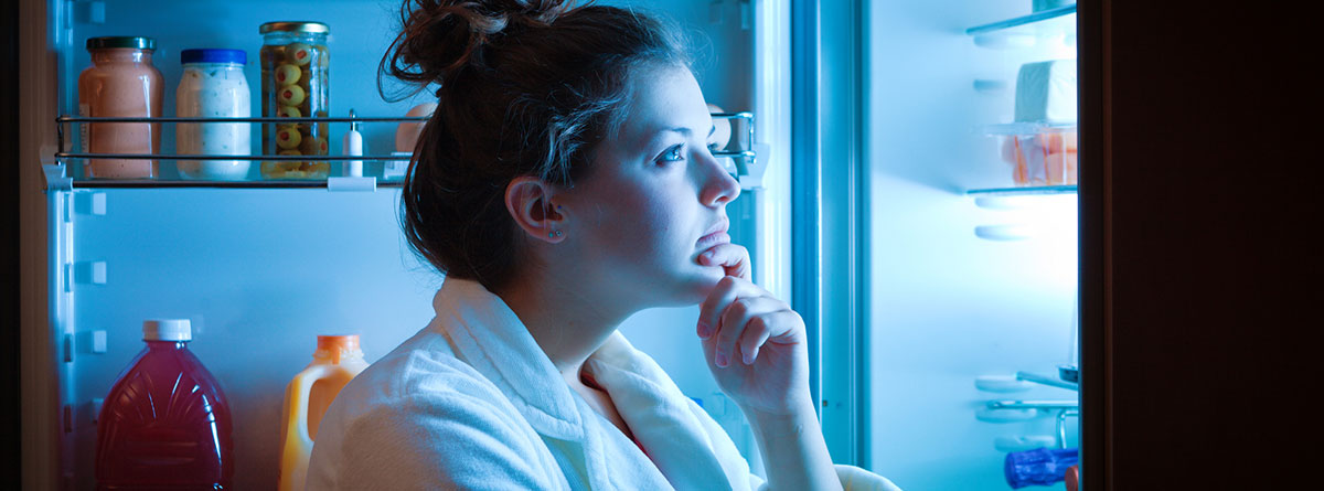 Hambre emocional: chica joven de noche con la puerta del frigorífico abierta mirando los alimentos