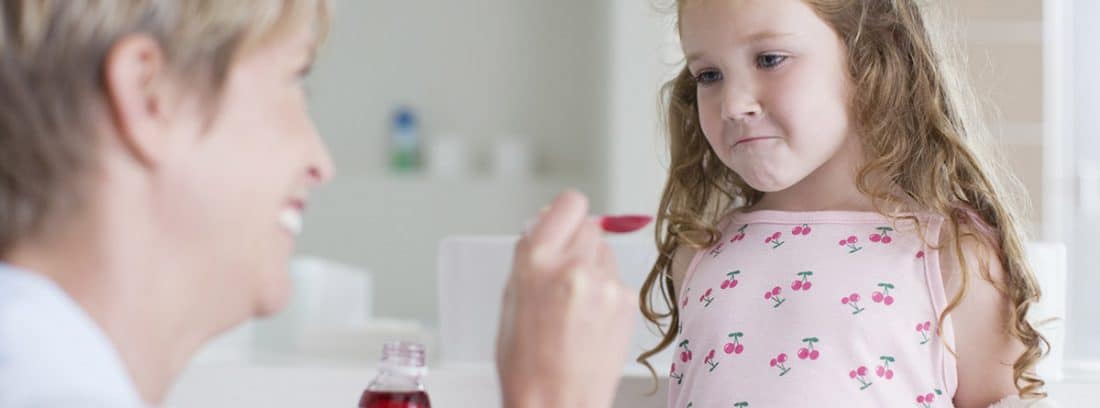 Uso correcto de medicamentos en niños: niña tomando una cucharada de jarabe