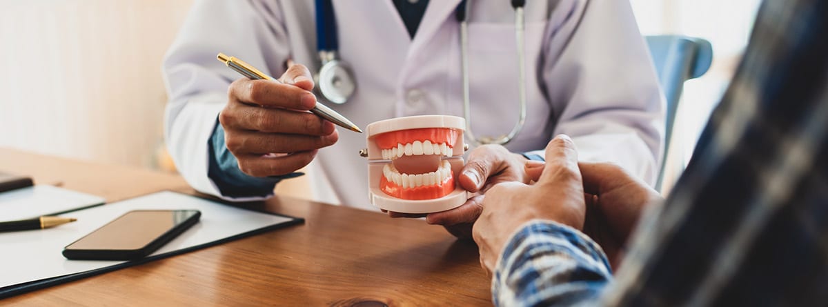 ¿Por qué se retraen las encías?: médico explicando a paciente las enfermedades de las encias con una dentadura artificial en la mano