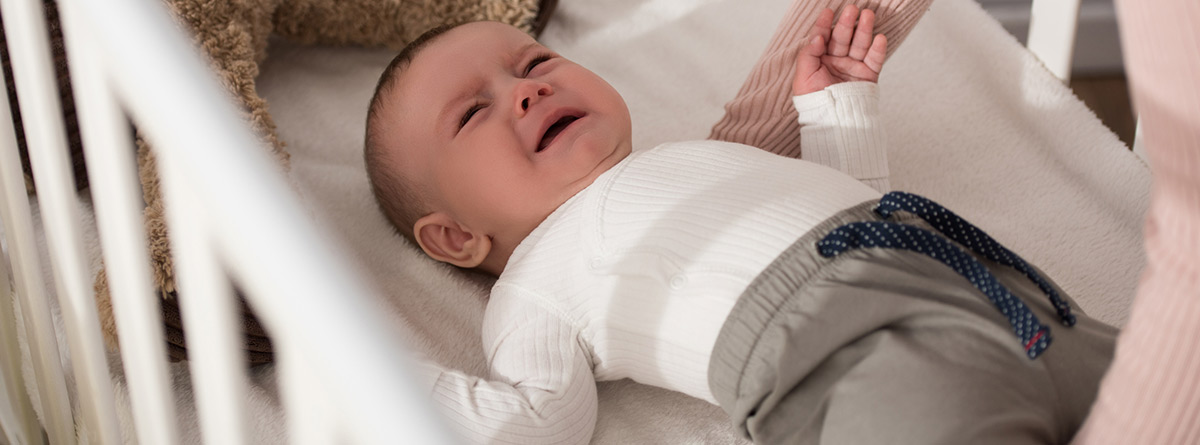 Síndrome de la cuna con pinchos: bebé encima de una cuna llorando y unos brazos de mujer intentando cogerlo