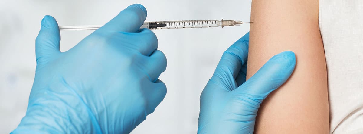 Eficacia y riesgos de la vacuna de la gripe: manos con guantes azules y con una jeringuilla pinchando en un brazo