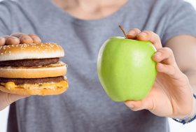Mujer con una hamburguesa en una mano y en la otra mano una manzana