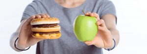 Mujer con una hamburguesa en una mano y en la otra mano una manzana