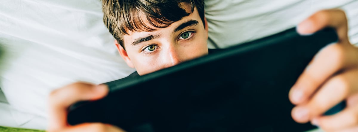 chico adolescente jugando en la cama con una consola de videojuegos