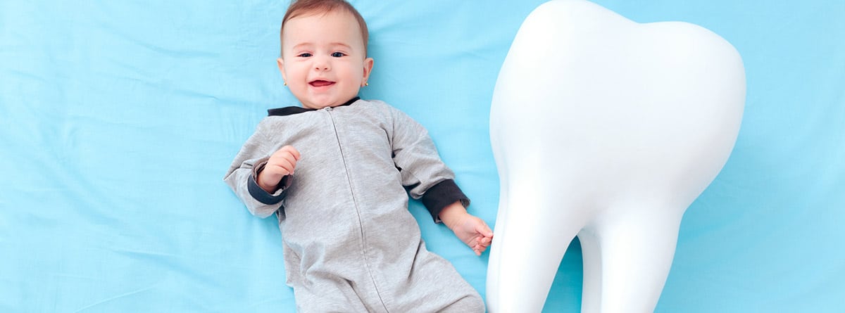 Cronología dental: bebé tumbado sobre fondo azul y un diente al lado