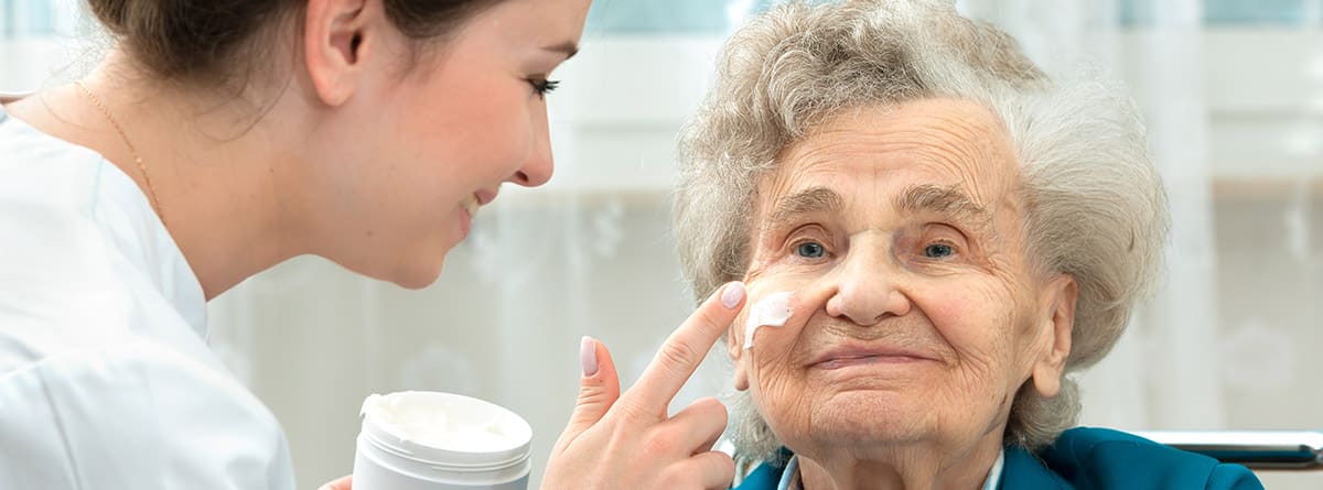 Prevención de enfermedades de la piel en personas mayores: Enfermera asiste a una anciana con medidas de higiene y cuidado de la piel en casa