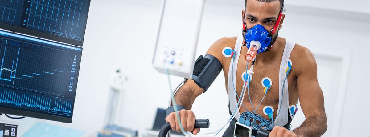 un atleta masculino en bicicleta en el ergómetro y realizando una prueba cardiopulmonar en la clínica.