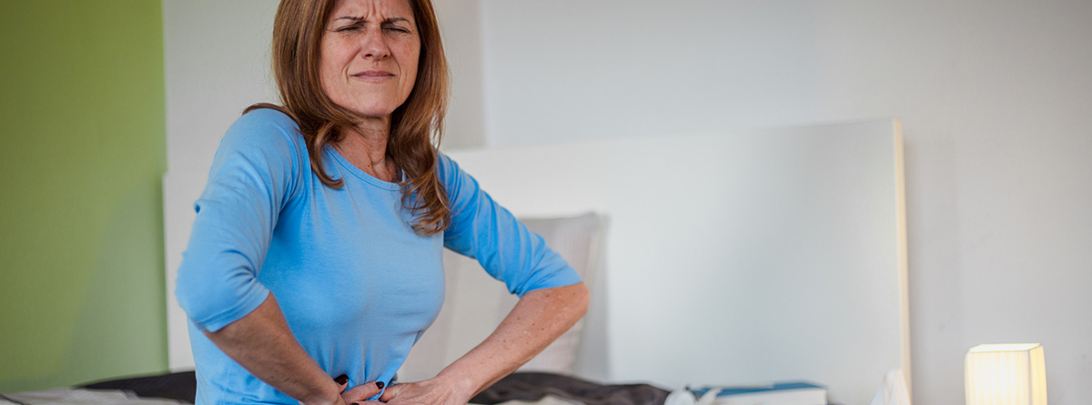 Pubalgia: mujer sentada en el sofá con las manos sobre las ingles y gesto de dolor