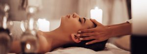 Terapias naturales: mujer tumbada en camilla dándose un masaje en la cabeza, con velas encendidas a los lados