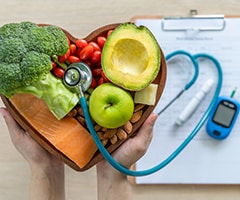 Alimentación para personas diabéticas: tabla de madera en forma de corazón con diferentes frutas y verduras encima de ella y un instrumental médico para medir el azúcar en sangre