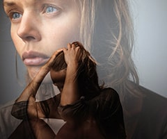 hipervigilancia en la ansiedad: mujer joven sentada con las manos en la cabeza sobre imagen difuminada de rostro de mujer