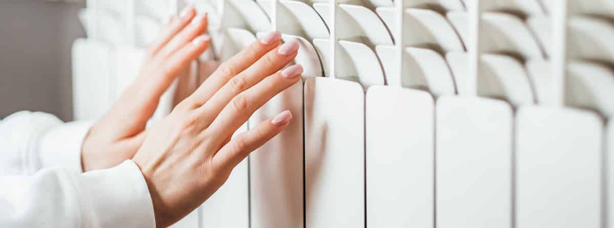¿Por qué tenemos las manos frías?: manos de mujer calentándose en un radiador