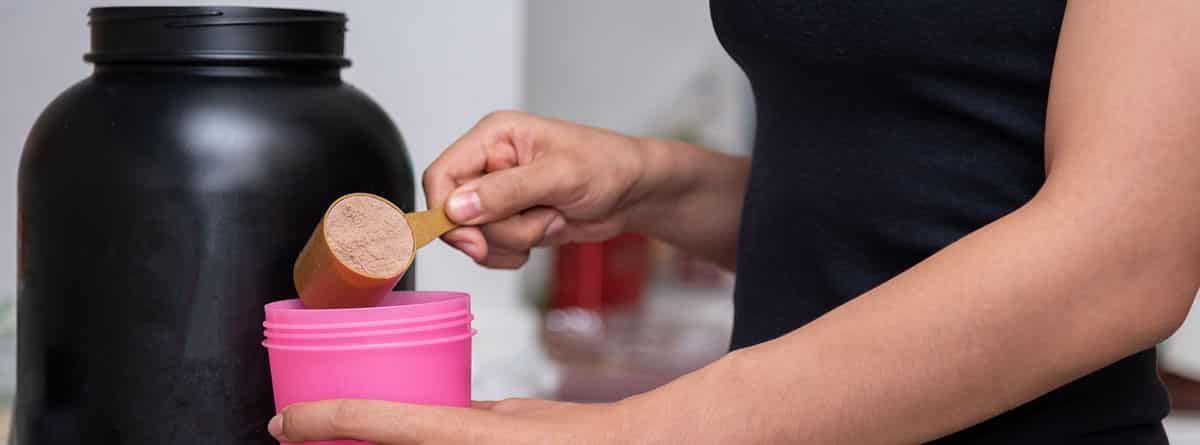Son buenos los batidos de proteínas: mujer echando un cacito de polvo de proteína en un vaso de batido