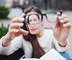 Miopía: mujer con gafas en la mano mirándolas de lejos