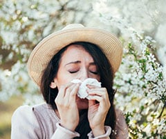 Alergia estacional: mujer con un sombrero de paja y un pañuelo en la naríz rodeada de plantas con polen