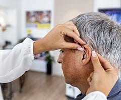 ¿Qué tipos de sordera existen?: paciente en consulta de especialista poniéndose un aparato para la sordera