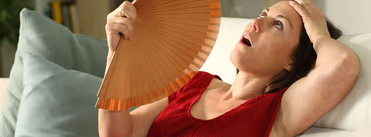 Sudores nocturnos: Mujer adulta abanicando sufriendo un golpe de calor sentada en el salón de casa
