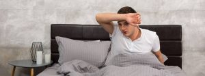 ¿Por qué se producen los sudores nocturnos: Un joven secándose el sudor de la frente en un dormitorio