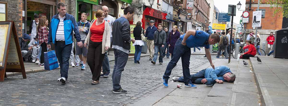 Intoxicación etílica: hombre tirado en el suelo, gente alrededor y una persona ayudando