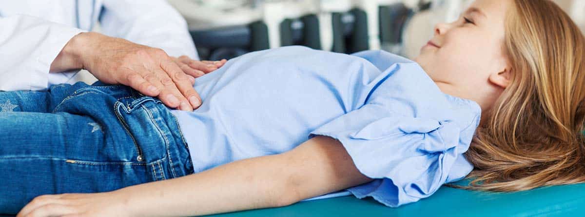 Nueva hepatitis infantil: niña tumbada en camilla y médico auscultando el abdomen