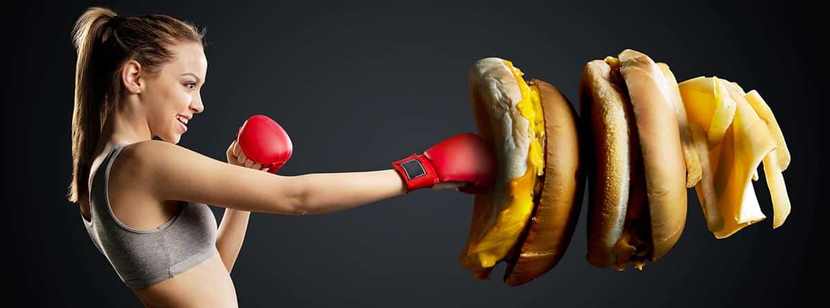Alimentos para reducir la inflamación: mujer con unos guantes de boxeo dando a productos calóricos
