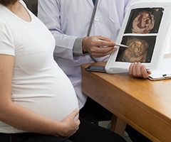 Ecografía 4D: Doctor sosteniendo el resultado de la imagen de ultrasonido 4D y hablando con la mujer embarazada.