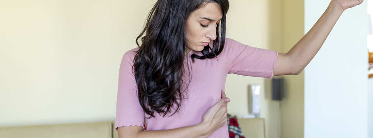 Erupción debajo del pecho, causas y tratamiento: mujer joven con camiseta rosa poniendo una mano debajo del pecho