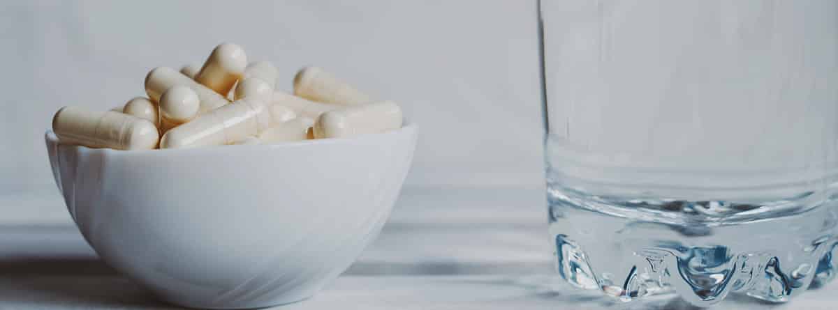 Beneficios de la lactoferrina: bol con cápsulas de lactoferrina y un vaso de agua al lado