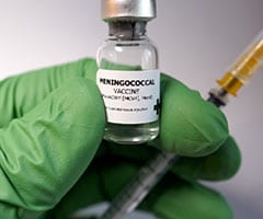 Vacuna contra la meningitis ¿Cuándo se administra?: manos con guantes verdes sujetando un vial de vacuna de la meningitis