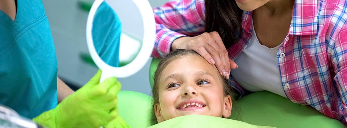 Sellado de piezas dentales: niña en consulta del odontólogo mirándo una lupa