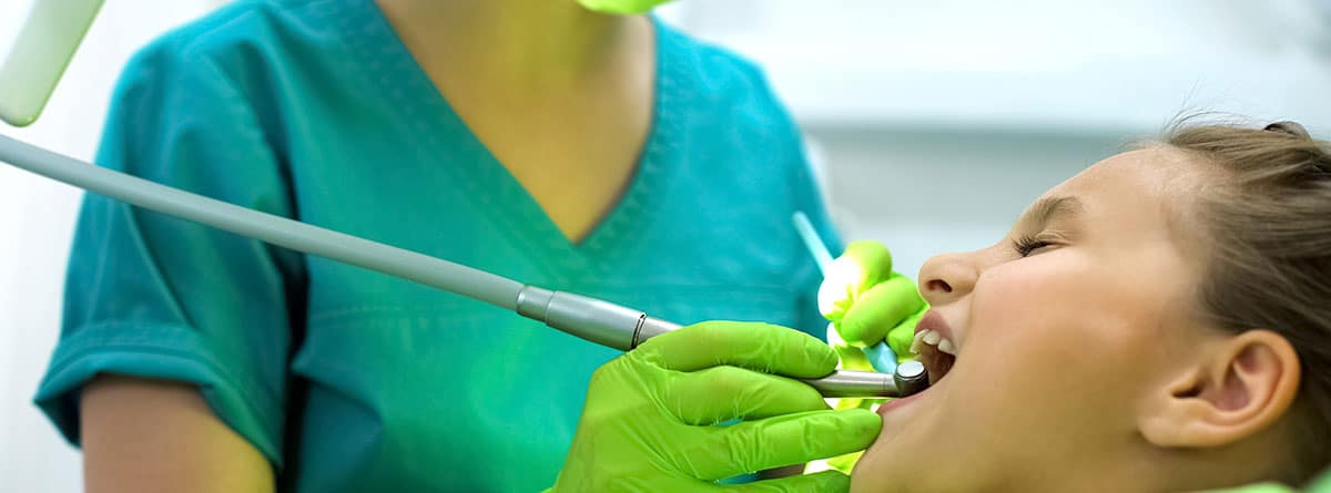 ¿Cómo se realiza el sellado de fisuras dentales?: Señora estomatóloga puliendo el esmalte dental de la niña