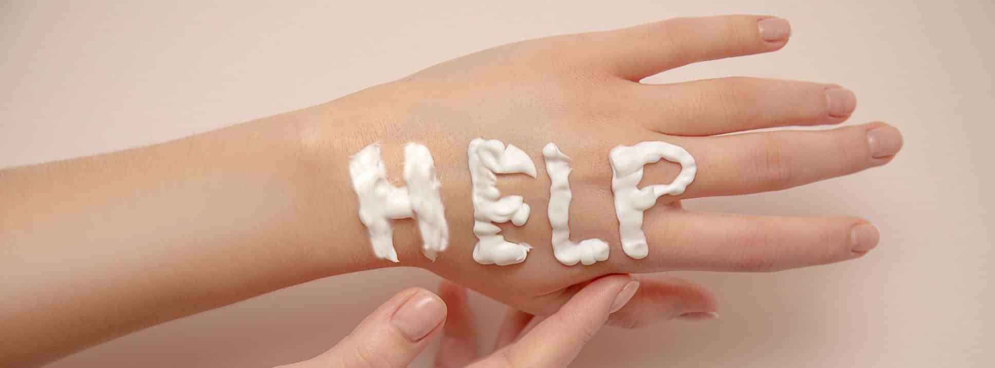 Cuidados de la piel en invierno: manos de mujer con la palabra ayuda en inglés realizada con crema