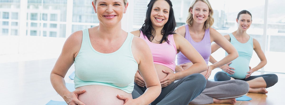 Mujeres embarazadas en clase de yoga sentadas sobre colchonetas 