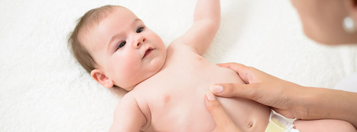 Espasmos infantiles: bebé tumbado y unas manos dando masaje