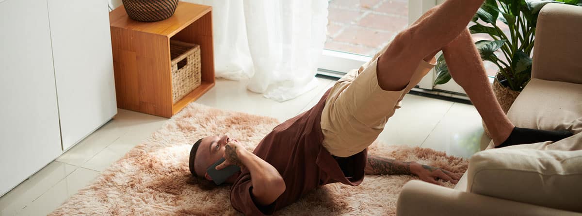 Suelo pélvico, ejercicios: Joven hablando por teléfono, apoyándose en el sofá cuando hace ejercicios en su casa