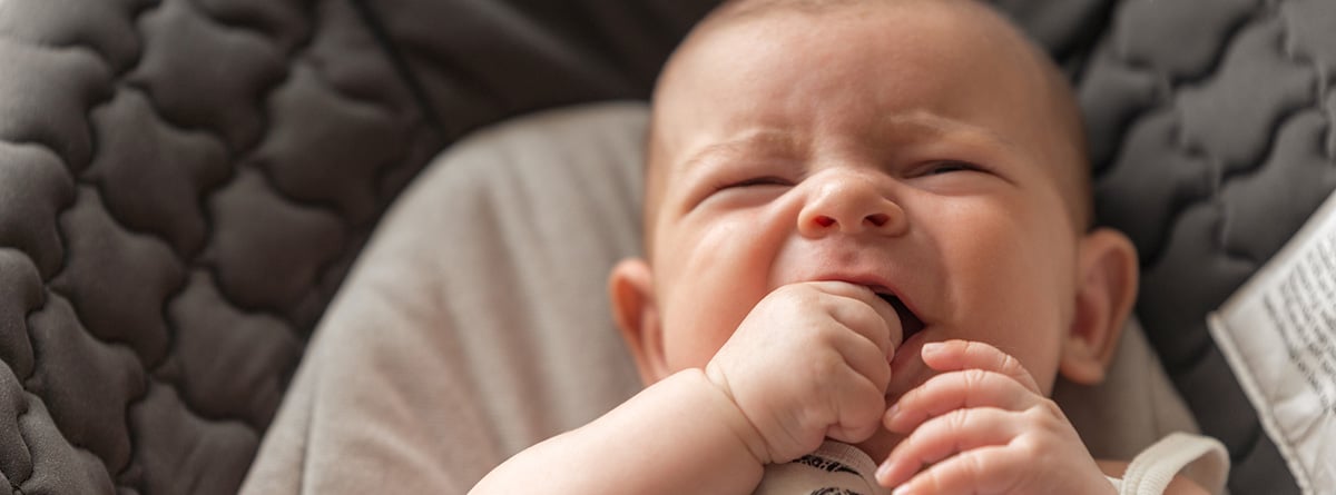 Dentición y fiebre en bebés: Bebé acostado y llorando con los dedos en la boca