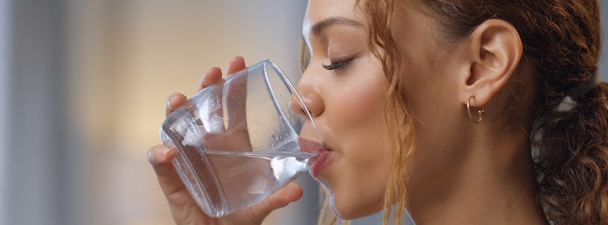 Cuánta agua hay que beber al día: chica joven bebiendo un vaso de agua