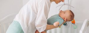 10 trucos y consejos para dormir a un bebé: mujer tomando en sus brazos a un bebé dormido para tumbarlo en una cuna