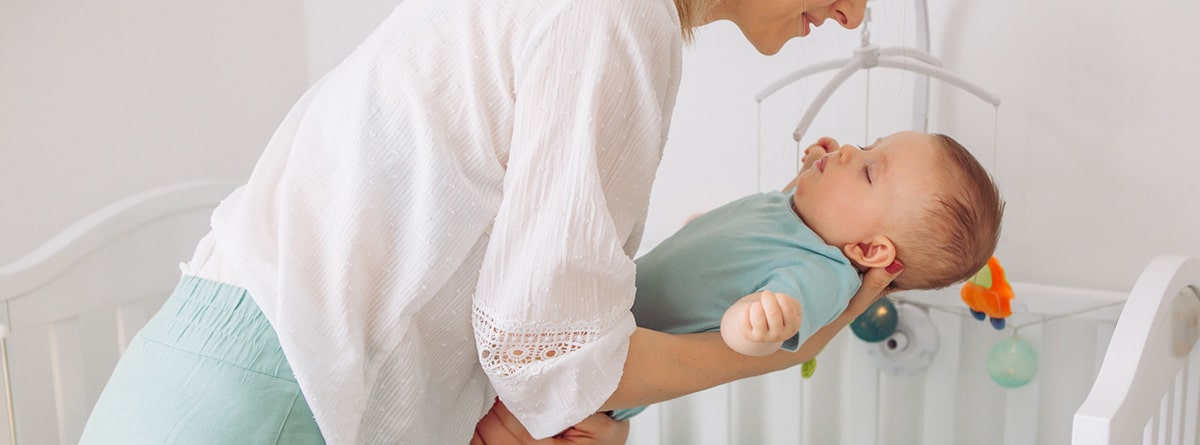 10 trucos y consejos para dormir a un bebé: mujer tomando en sus brazos a un bebé dormido para tumbarlo en una cuna