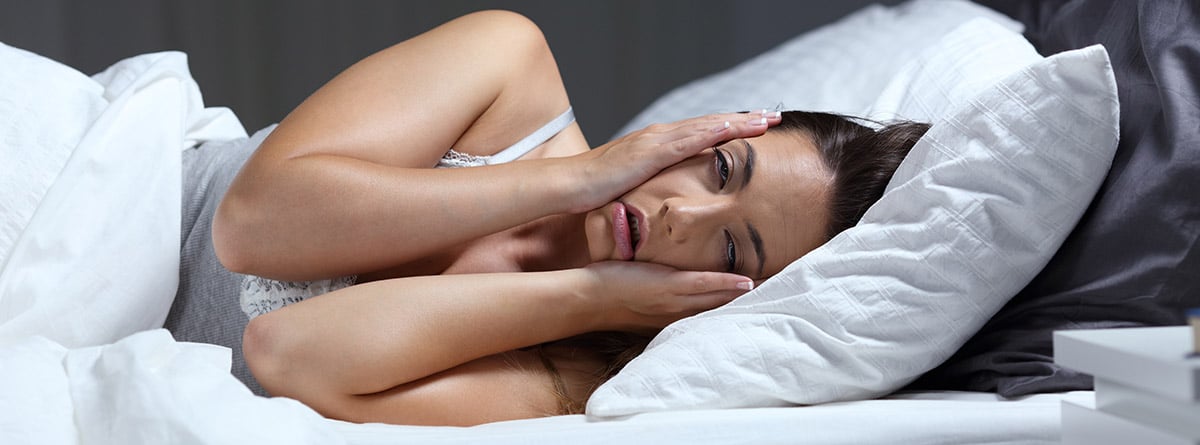 ¿Por qué estoy cansado pero no puedo dormir?: mujer en la cama con las manos sobre la cara sin poder dormir