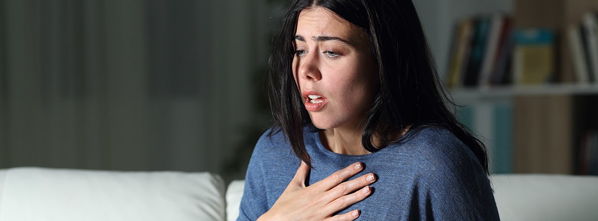 Depresión y ansiedad: mujer sentada en el sofá con la mano en el pecho, con respiración rápida