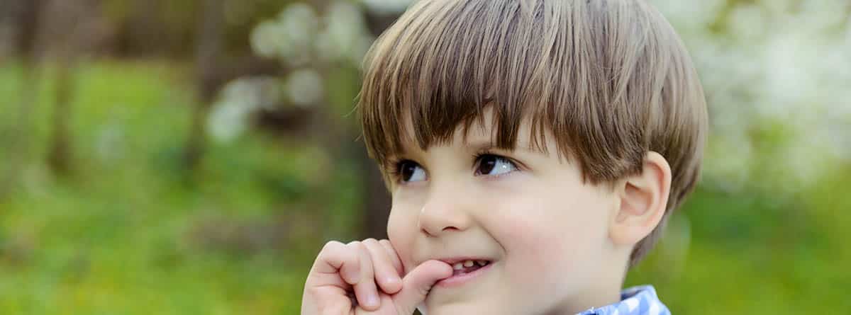 Morderse las uñas: niño moreno en el campo mordiéndose las uñas