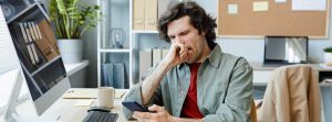 Cómo vencer a la procrastinación: un joven caucásico bostezando en el lugar de trabajo de oficina y navegando por las redes sociales por teléfono