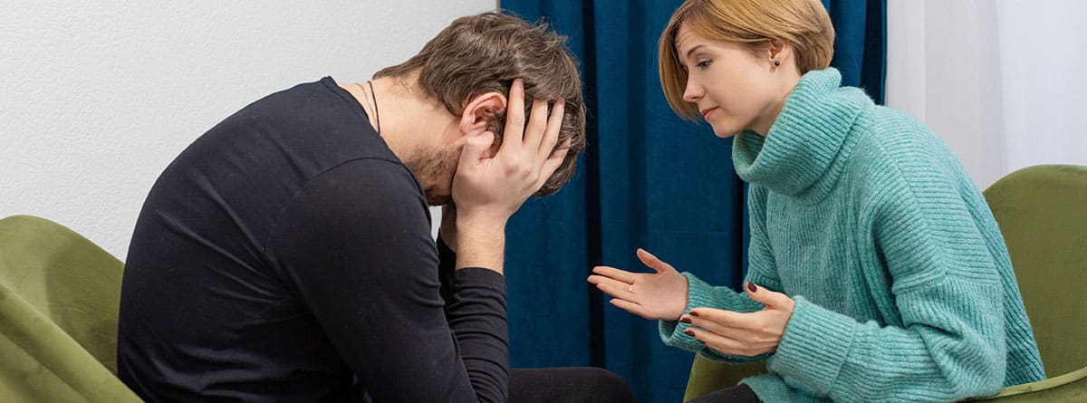 ¿Cómo actuar ante un ataque de ansiedad?: hombre con las manos en la cabeza delante de una mujer psicóloga con los brazos abiertos