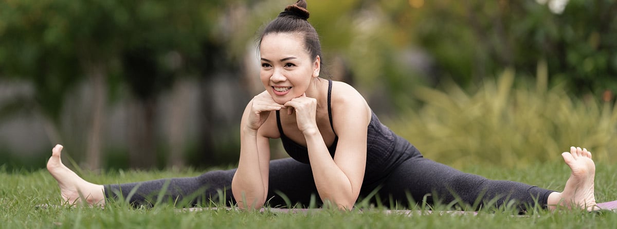 mujer realizando estiramientos con las piernas abiertas en el campo