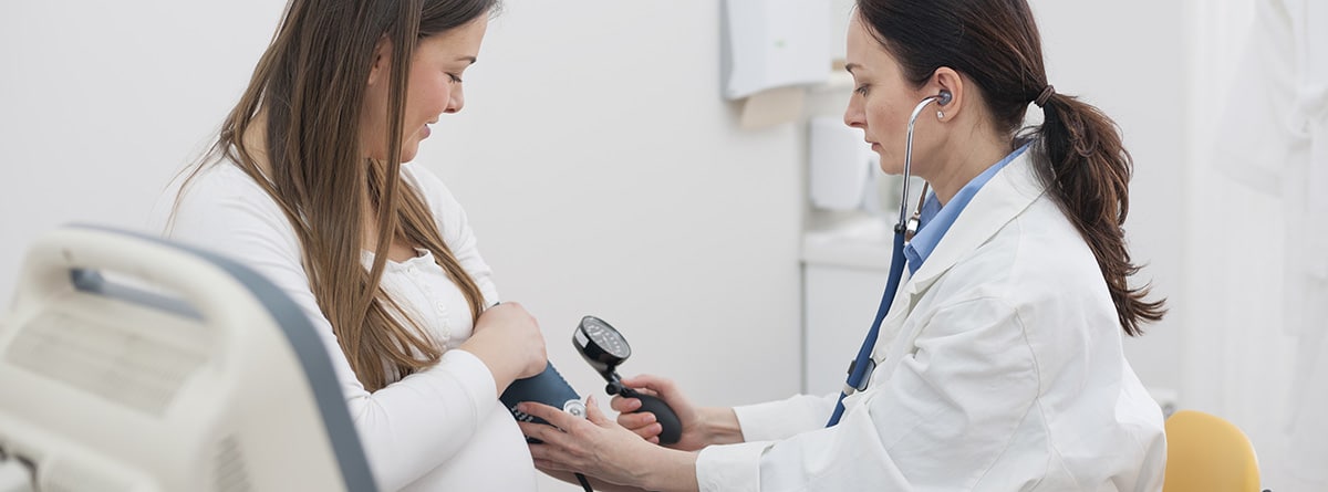 Tensión alta en embarazo:Mujer embarazada en el consultorio médico, médico midiendo la presión arterial