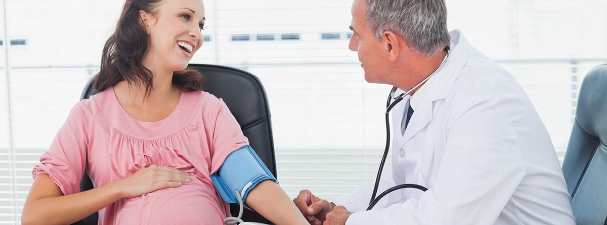Médico tomando la presión arterial de una paciente embarazada sonriente 