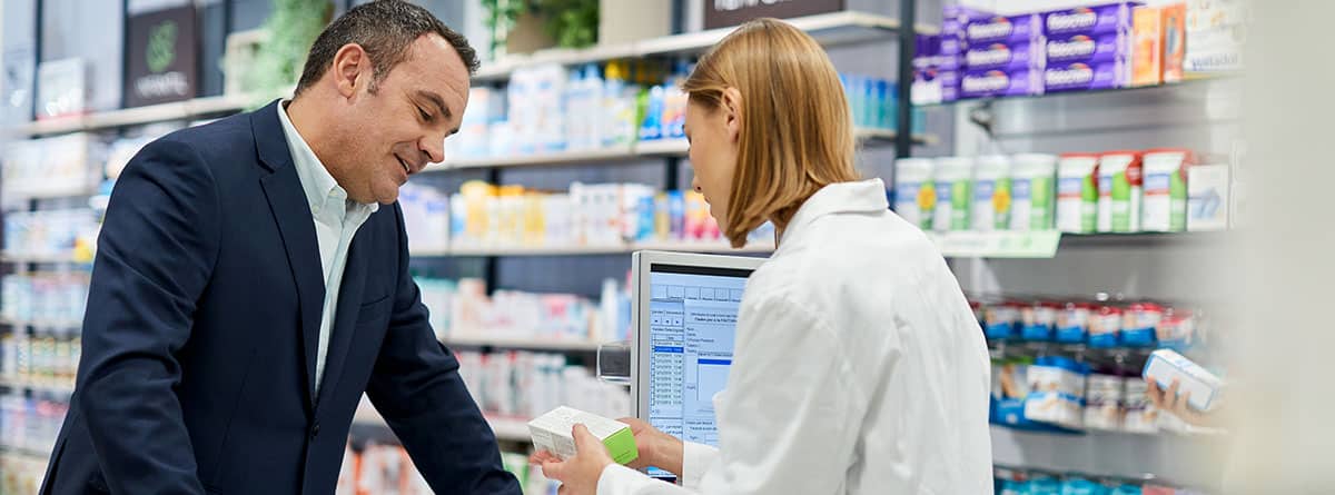 Qué son los alfabloqueantes y para qué sirven: dependienta de farmacia explicando a un hombre el medicamento para la próstata